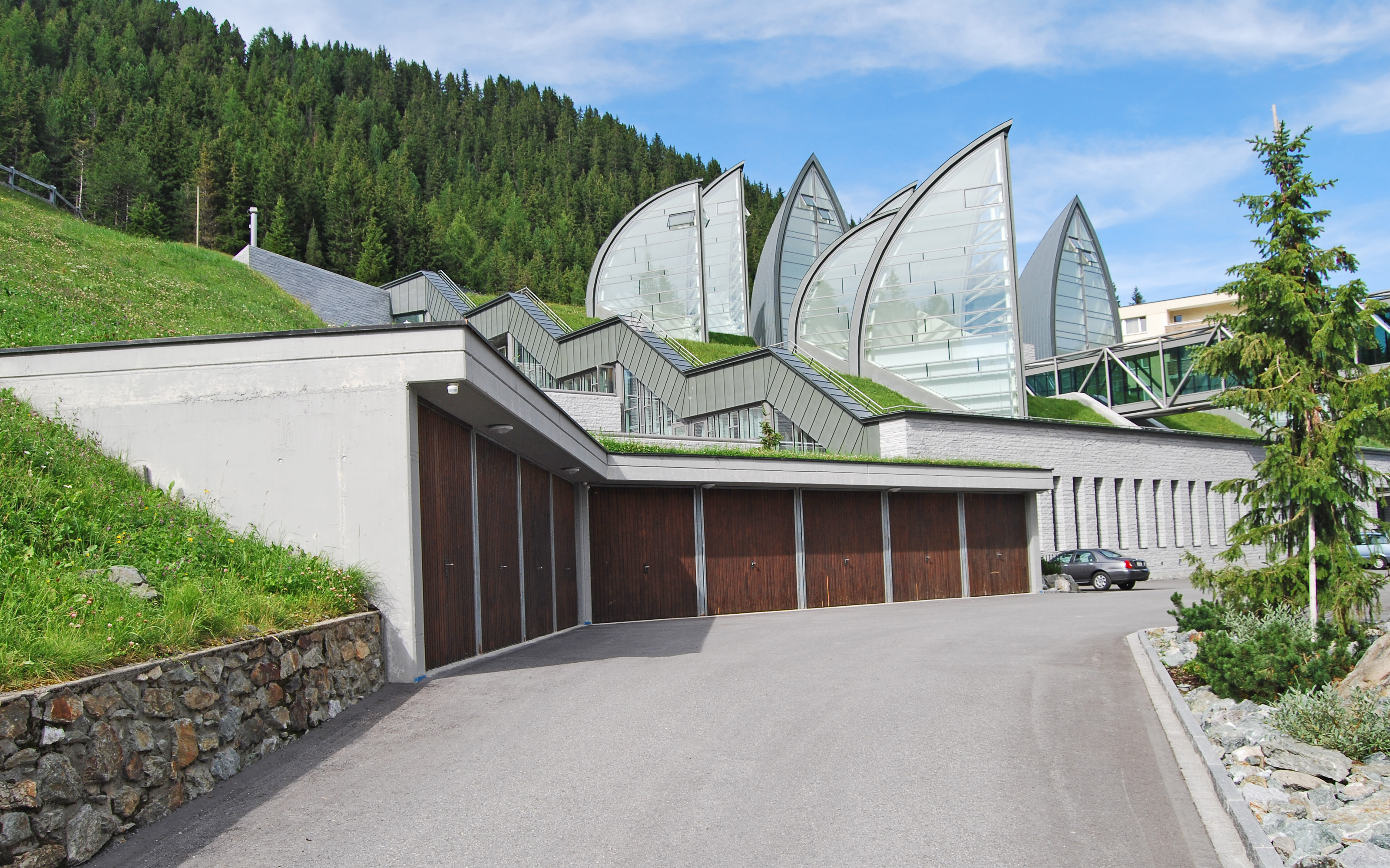 Most of the structure of the building is built into the hillside. Pitched green roof with lawn and sail-shaped skylights